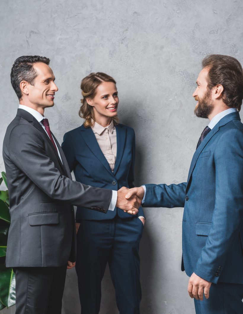 side view of smiling business people shaking hands with colleague standing near by